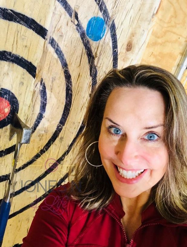 Neile Jones stands next to the target for an indoor axe throwing facility.